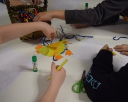 Na białym stoliku leży pokazowa kura wielkanocna, którą dzieci odwzorowują na swoich szablonach.