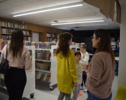 Bibliotekarka tłumaczy dzieciom zasady gry, podczas której muszą znaleźć ukryte w bibliotece jajka.