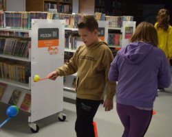 Dzieci mijają się w zawodach, podczas których przenoszą na łyżkach plastikowe jajka