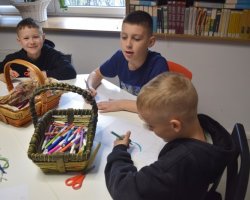 Trzech chłopców wykonuje pracę plastyczną. Na stoliku, przy którym siedzą znajdują się koszyku z mazakami.
