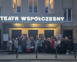 Grupa czytelników pozuje do zdjęcia stojąc przed budynkiem. Nad ich głowami widnieje napis Teatr Współczesny